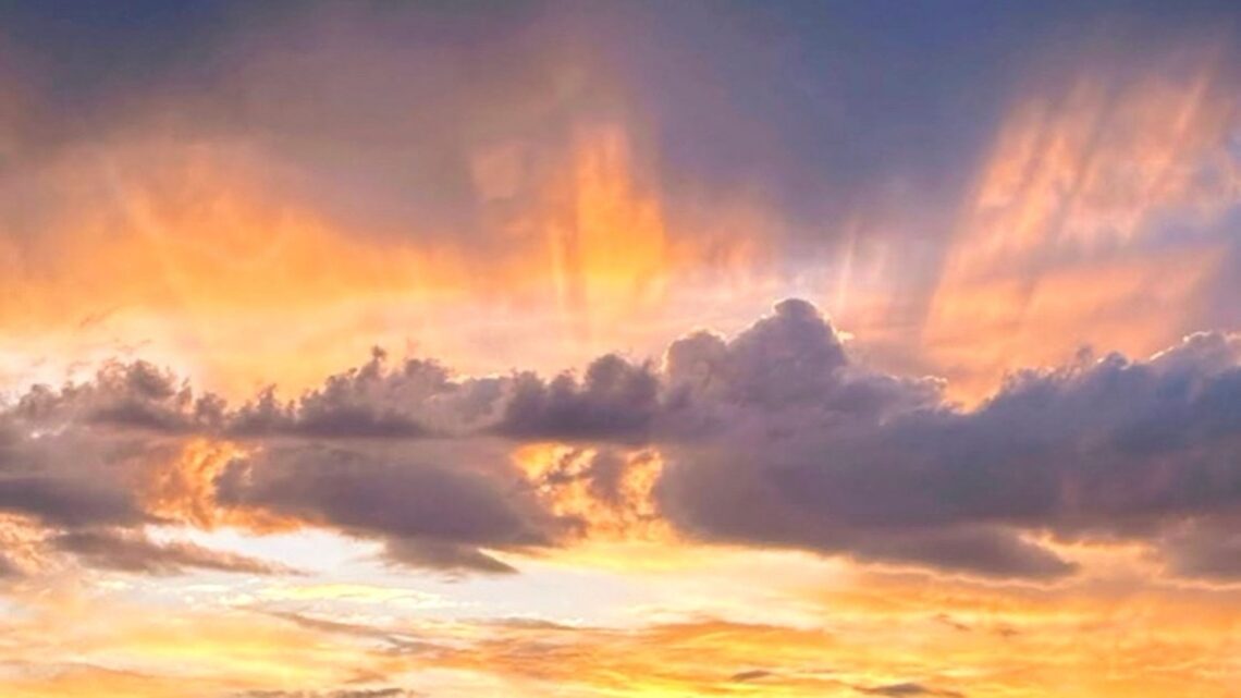 Soft golden sunset breaking through layered clouds over a quiet horizon, symbolizing calm, reflection, and clarity